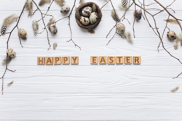 Quail eggs and feathers in the nest and wooden text for Happy Easter