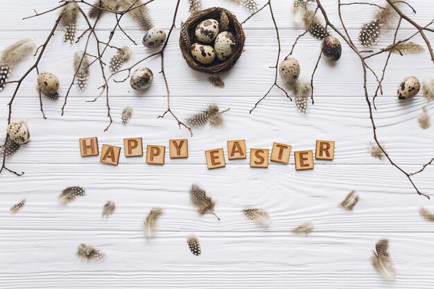 Quail eggs and feathers in the nest and wooden text for Happy Easter 