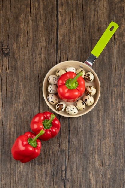 Quail eggs on frying pan and bell peppers on wooden surface