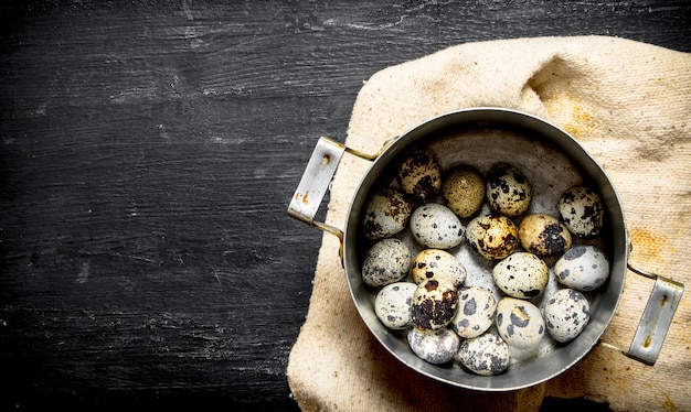 Quail eggs in an old pot. On a black wooden table.