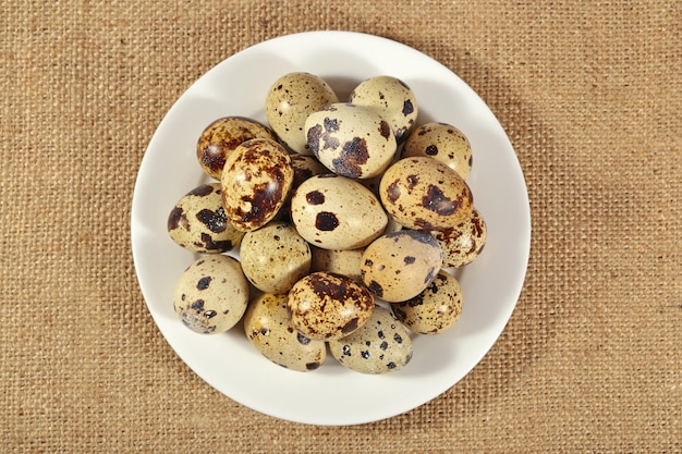 Quail eggs in a white bowl in a sacking background