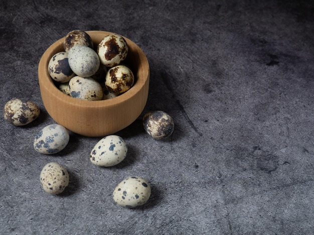 Quail eggs in a wooden bowl On a dark concrete background Top view Free space for copying