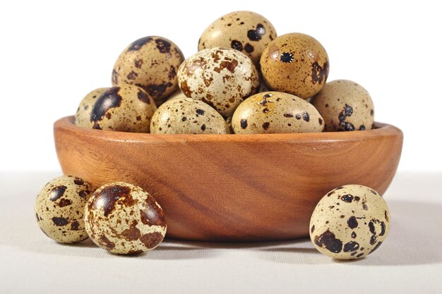 Quail eggs in a wooden bowl on a white background