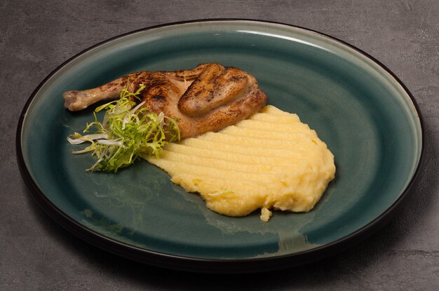 Quail with mashed potatoes on a green plate on a gray background