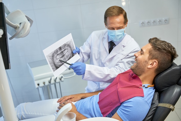 Квалифицированный стоматолог и его молодой пациент обсуждают рентгеновский снимок