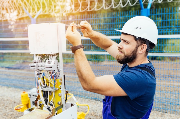 A qualified electrical engineer sets up a control and measuring\
device at an industrial facility on a summer day