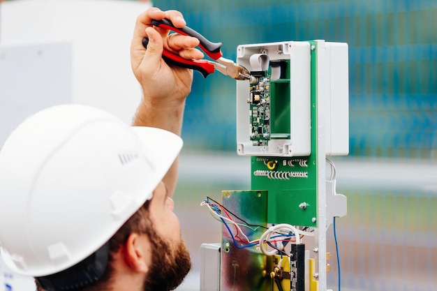 A qualified electrical engineer sets up a control and measuring device at an industrial facility on a summer day