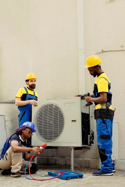 Qualified electricians installing condenser for client after replacing broken unit. Professional workers enlisted to optimize new HVAC system's performance, ensuring it operates at maximum capacity