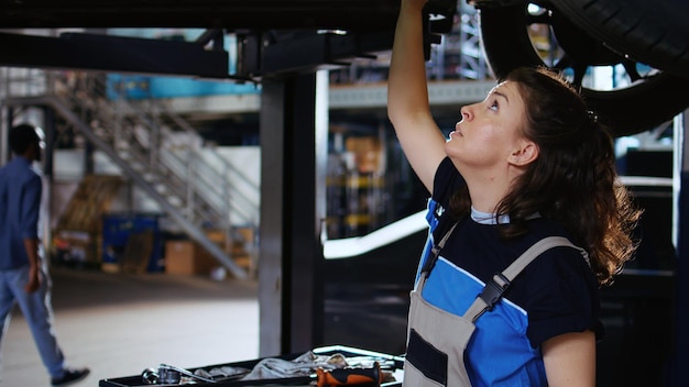 Qualified engineer working on suspended car in garage changing tires during routine maintenance Auto repair shop employee underneath vehicle looking to fix potential issues