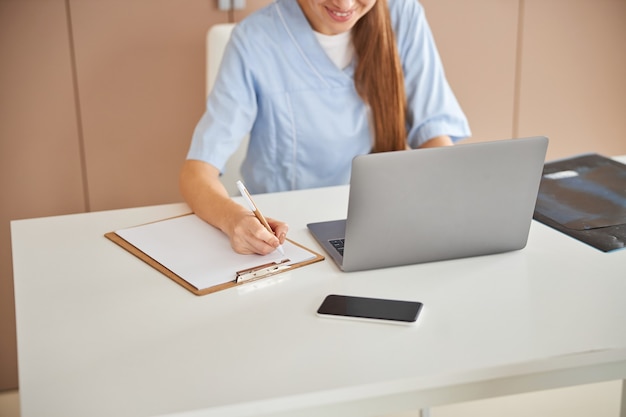 Qualified female doctor writing notes and smiling