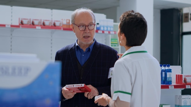 Фото Квалифицированный фармацевтический врач помогает пожилому человеку с медицинскими советами пожилой клиент в аптеке, желающий купить антибиотики, регулирующие сердцебиение, просит эксперта о руководстве