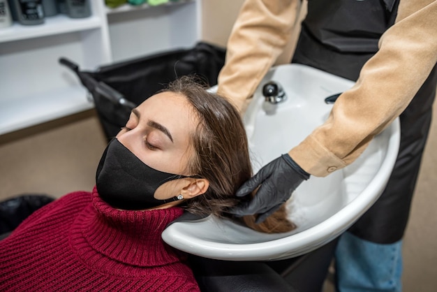 A qualified serious steamer prepares his regular client to wash\
his head in a new quality salon during a pandemic the concept of\
procedures with hair beauty salon concept
