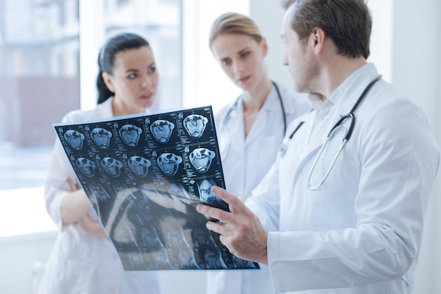 Qualified smart concentrated radiographs working at the laboratory and having discussion while holding computed tomography photo