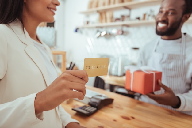 Quality service. The focus being on the hands of a beautiful young woman holding a golden card and being ready to pay for her order in the coffeehouse