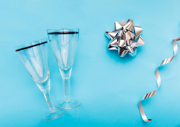 Photo quality two empty clean glasses for drinks on a clear blue background with a silver foil bow