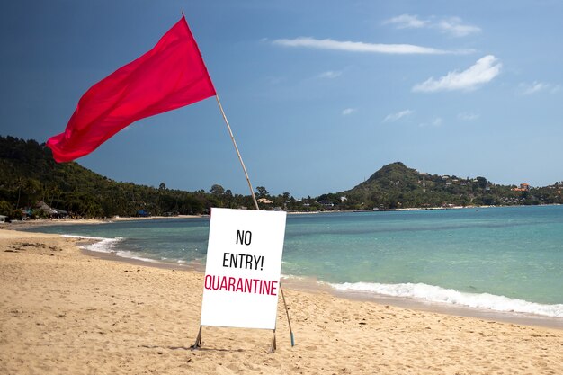 quarantaineconcept, gesloten grenzen, vakantieannulering. tropisch strand op een zonnige dag zonder mensen. er is een rode vlag en een bord met de vermelding geen inreisquarantaine.