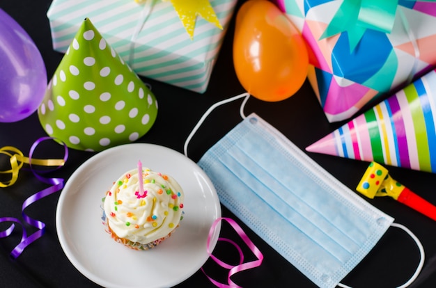 Quarantine birthday in isolation. Birthday cupcake, face mask, gifts and holiday accessories.