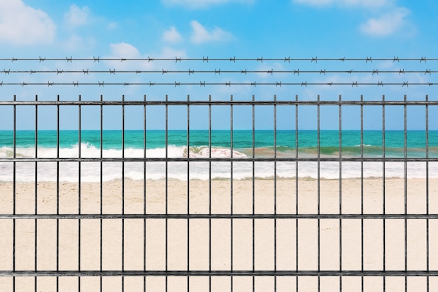 Quarantine due to Novel Coronavirus COVID-19 2019 n-CoV Concept. Metal Fence with Barbed Wire in front of Sand Ocean Beach extreme closeup. 3d Rendering