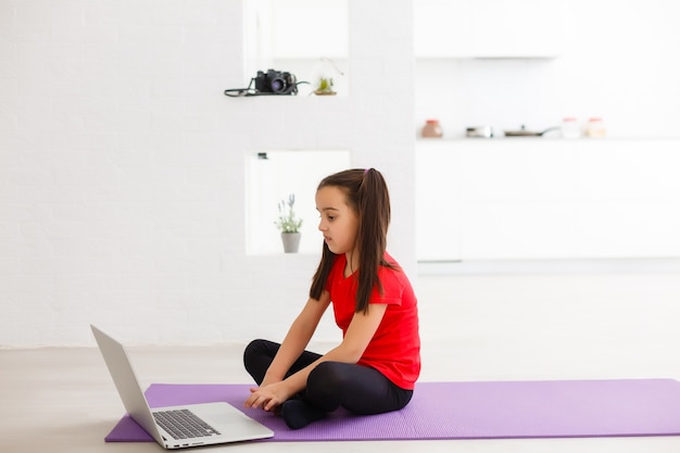 Quarantine at home. little girl doing yoga olnline on a laptop during self isolation quarantine