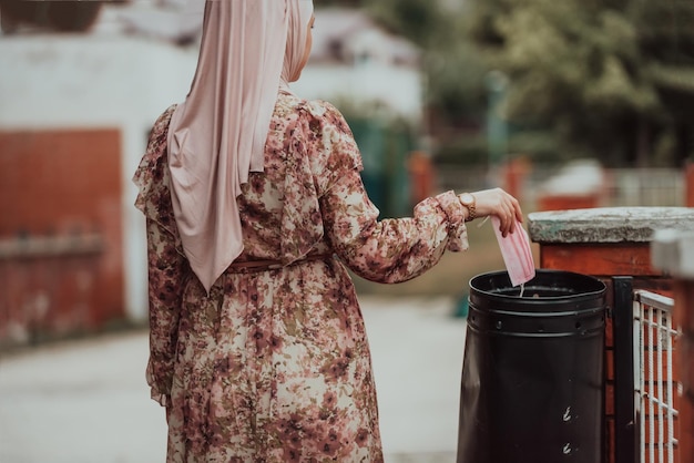 Quarantine is over concept Muslim Woman throwing away protective face mask to garbage trash can on background of blooming parkEnd of covid19 pandemicfreedomvictorywin High quality photo