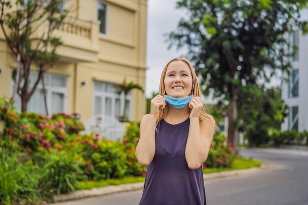 検疫は、私たちがいる小さな町の家を背景にマスクを脱ぐコンセプトの女性です