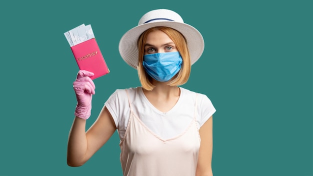 Quarantine prevention Travel restriction Woman in summer outfit protective mask pink gloves holding foreign id with tickets Looking at camera isolated on green Pandemic measures Holiday trip