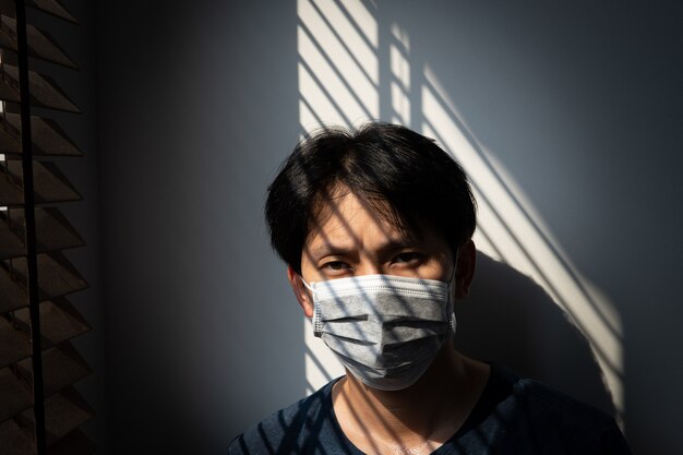 Quarantine of risky people to prevent COVID-19 spreading, Man wearing mask and looking out on the window at home, Corona virus. Wuhan coronavirus and epidemic virus symptoms and protection