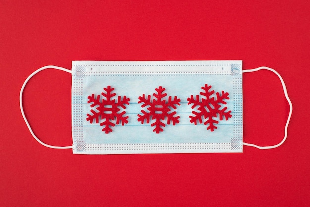 Quarantine and winter holidays concept, Top above overhead view close up photo of medical mask and decorative red snowflakes on it isolated on red background