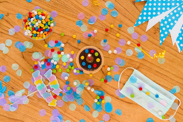 Concetto di compleanno in quarantena. covid19. maschera chirurgica, cioccolatini, coriandoli e articoli per feste sparsi sul tavolo. vista dall'alto