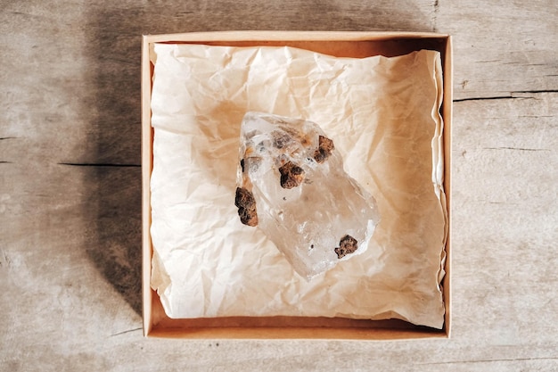 Quartz crystal in a kraft paper box on wooden background. Top view. Copy, empty space for text