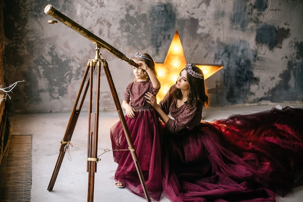 The queen and her daughter Princess looking at the stars through a telescope in the loft