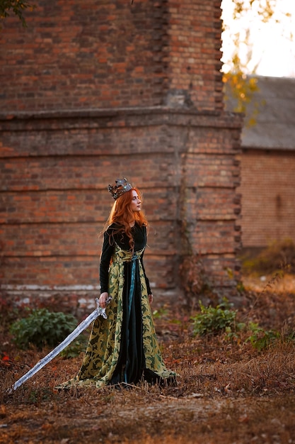 Foto regina dai capelli rossi in un abito verde con una corona e una spada