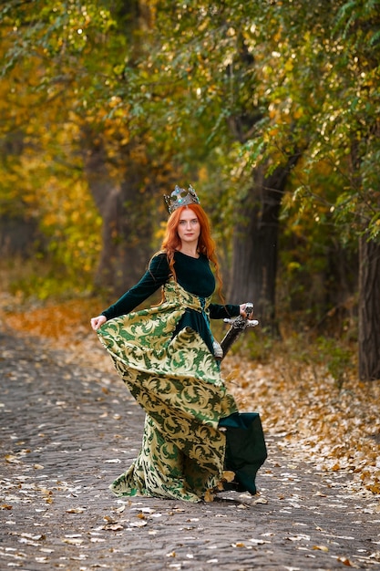 사진 숲에서 왕관과 함께 녹색 드레스에 빨간 머리를 가진 여왕