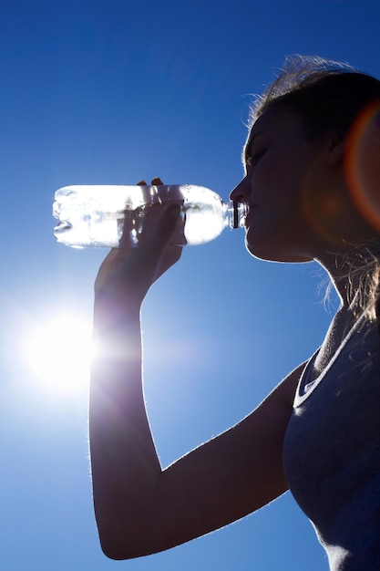 喉の渇きを癒す青い空を背景に水を飲む女性の低角度のシルエットショット