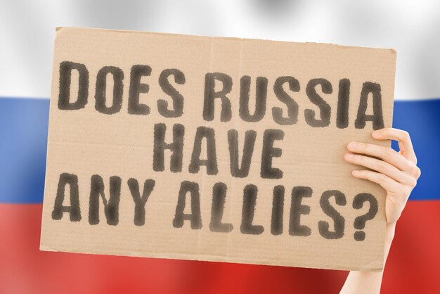 The question " Does Russia have any allies? " on a banner in men's hand with blurred Russian flag on the background. Politics. Diplomacy. Relationship. Relation. Military. Parliament. Relations. State