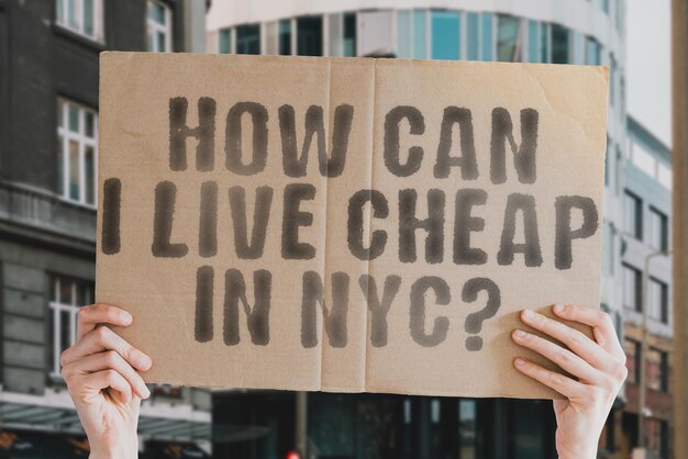 The question How can I live cheap in NYC is on a banner in men's hands with blurred background Choice Expenses Economy Live Financial Estate Economic Increase New York Money Rate