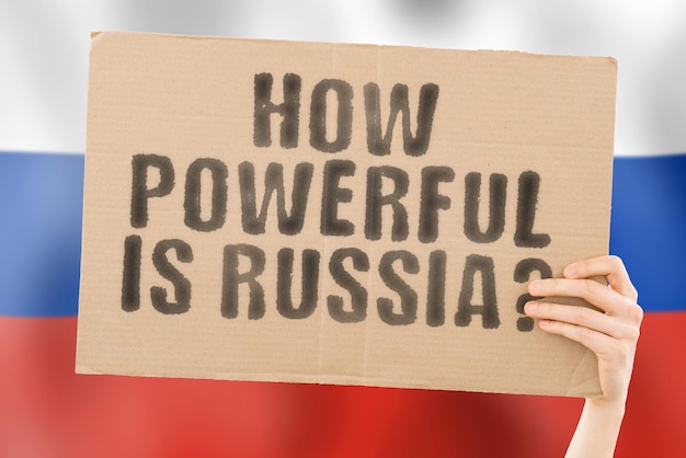 The question " How powerful is Russia? " on a banner in men's hand with blurred Russian flag on the background. Politics. Diplomacy. Military. Strong. Nuclear weapon. Strength. Armour. Demonstrate