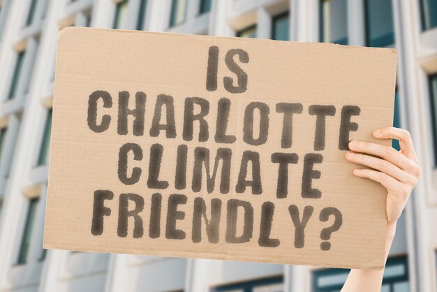 샬롯이 기후 친화적인가라는 질문은 배경이 흐릿한 남성의 손에 있는 배너에 있습니다. 지원 팀 활동가 도시 일몰 탄소 생태 에너지 새로운 청정 온난화 폐기물