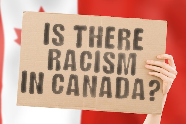 The question Is there racism in Canada is on a banner in men's hands with a blurred Canadian flag in the background Interracial Issues Justice Nation Politics Peace Patriotism Rebellion