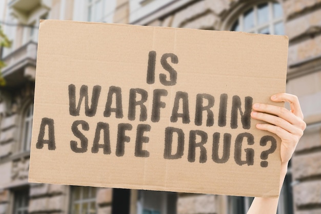 The question Is warfarin a safe drug is on a banner in men's hands with blurred background Safe Safety Formula Secure Science Security Poison Caution Danger Protect Carbon Chemistry