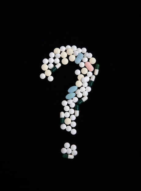 A question mark made of pills on a black background. the\
concept of vaccination and health protection