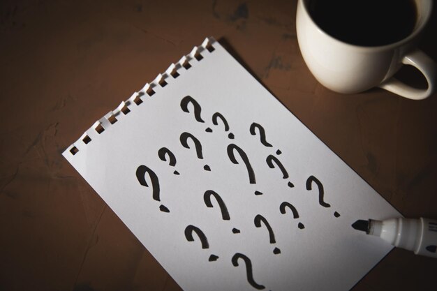 Question mark on notepad with coffee cup on table