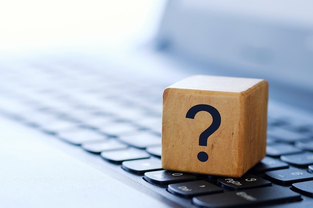 Photo a question mark on a wooden cube on a computer keyboard, with a blurred background and shallow depth of field.