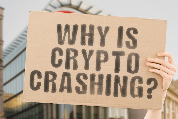 The question " Why is crypto crashing? " on a banner in men's hand with blurred background. Savings. Security. Encryption. Broken. Exchange. Bank. Damage. Bankrupt. Problem. Lose. Investment. Failure