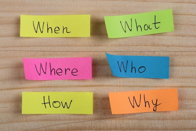 Photo questions why what where when why how on colorful stickers on wooden desk