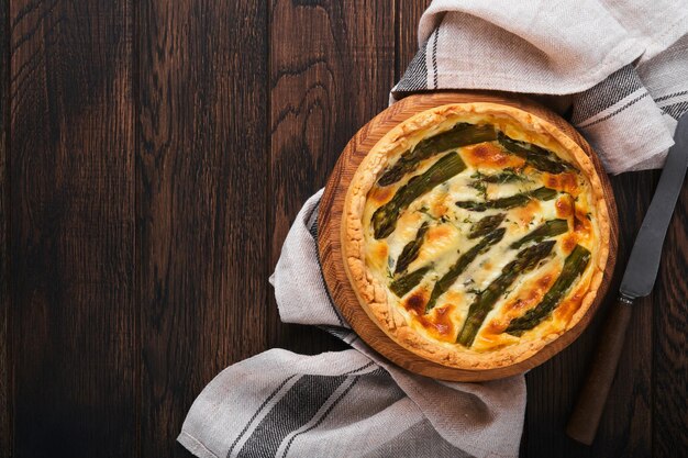 Quiche Homemade asparagus pie or quiche with cheese and spinach on old dark wooden table background Top view