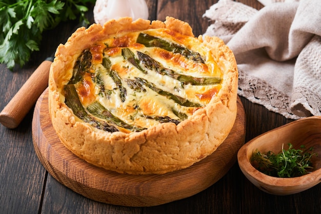 Quiche Homemade asparagus pie or quiche with cheese and spinach on old dark wooden table background Top view