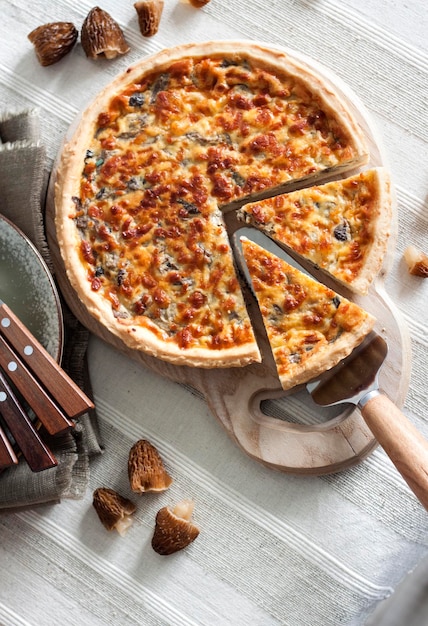 Quiche open tart pie with morel mushrooms onion and cheese on wooden cutting board