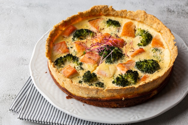 Foto quiche taart, bovenaanzicht. uitzicht van boven. klassieke quiche van zalm en broccoli gemaakt van korstdeeg met broccoliroosjes en gerookte zalm in een romig scharrelkoekje met vrije uitloop op tafel.