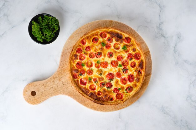 Quiche with chicken, cherry tomatoes and cheese. Appetizing open French pie. Dish on a wooden kitchen board. Top view.